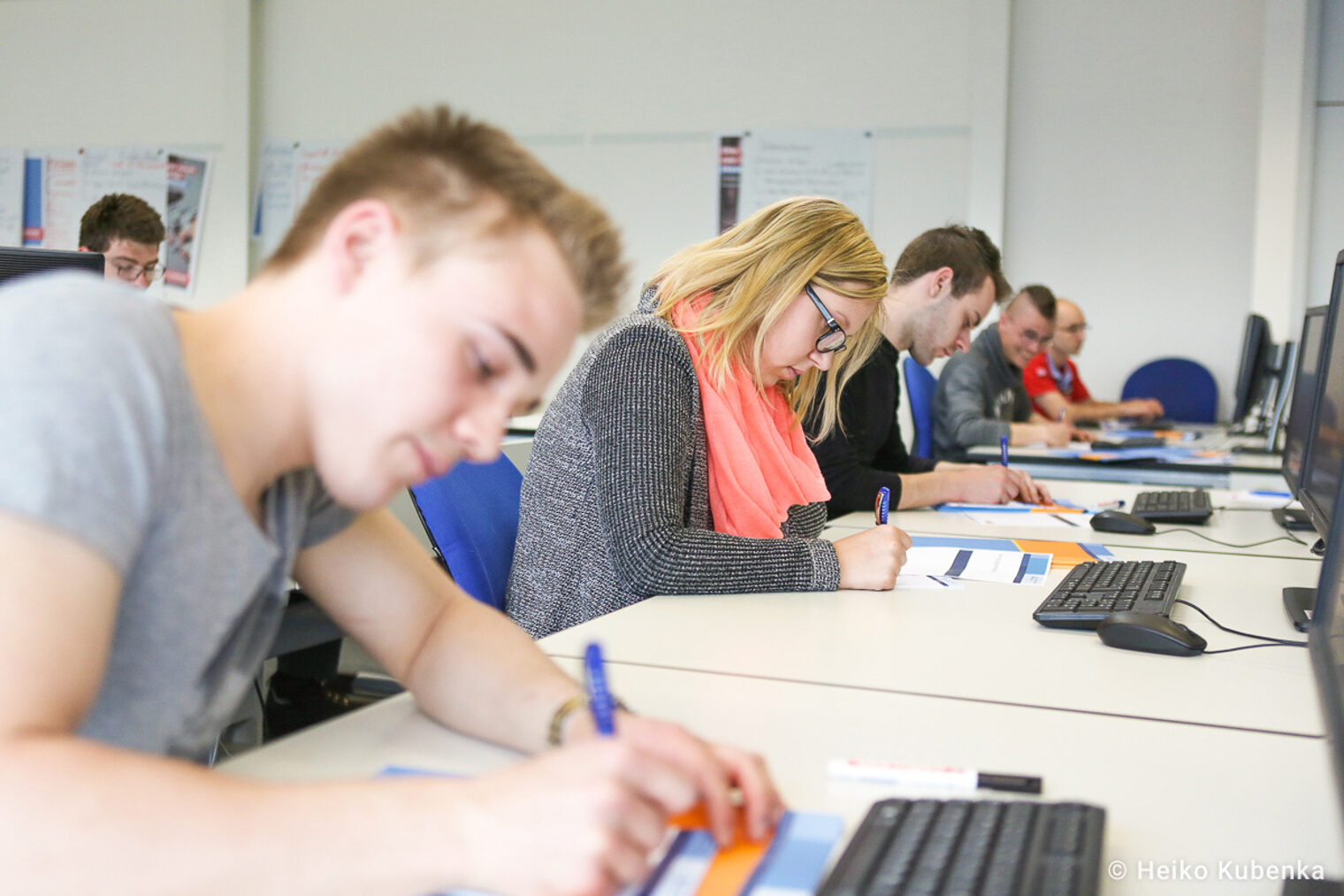 Teilnehmende eines Seminar schreiben auf Arbeitsblätter Auszubildende nehmen an einem Seminar teil und schreiben auf Arbeitsblätter, während sie vor Computern sitzen